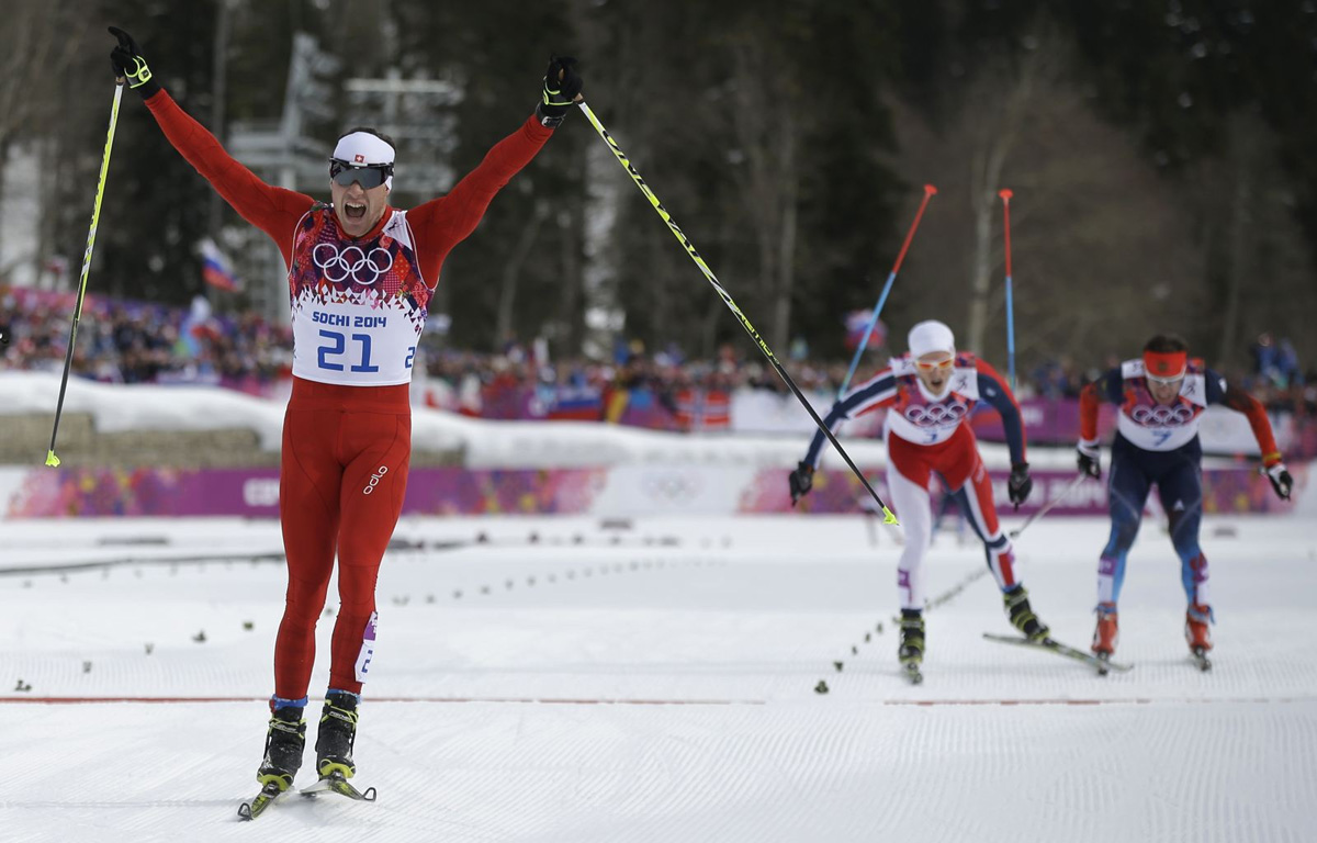 Скандальный финиш Максима Вылегжанина из России (справа) и норвежского лыжника Мартина Сундбю. На переднем плане победитель соревнований по мужскому скиатлону на 30 км швейцарец Дарио Колонья. 9 февраля 2014 года. (Фото AP Photo/Gregorio Borgia)